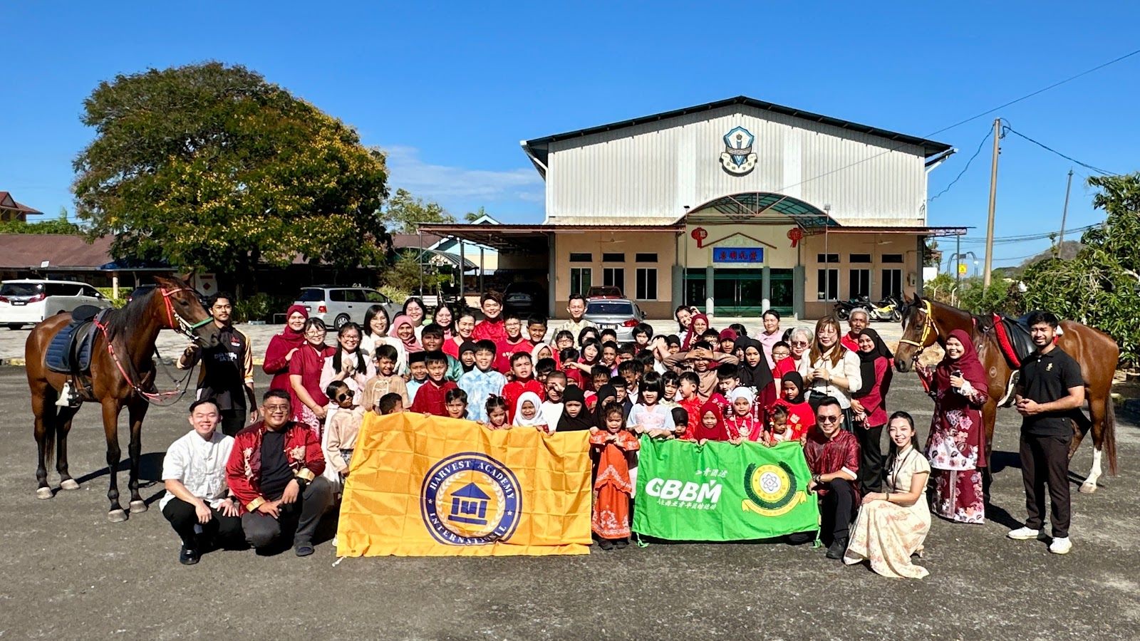 Students and teachers of SJKC Khay Beng with Harvest Academy and GBBM banners and horses on the school grounds