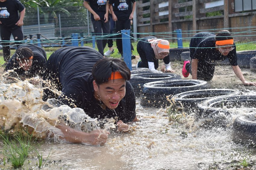 A student crawling through a muddy obstacle course at H-Explore